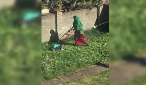 Une femme tente de passer la tondeuse dans son jardin
