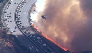 Un hélicoptère largue de l’eau sur une autoroute qui se fait attaquer par les flammes en Californie