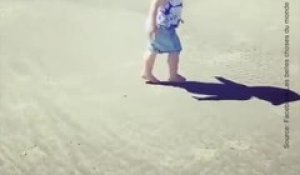 Un bébé joue avec son ombre sur la plage