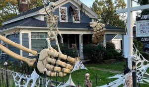 Cette décoration d'Halloween impressionnante représente un squelette gigantesque qui semble sortir d'une maison