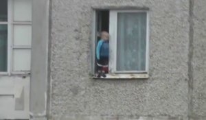 Un bébé joue sur le rebord d'une fenêtre au 8ième étage