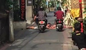 Un scootériste roule sur une personne allongé qui bloque la route