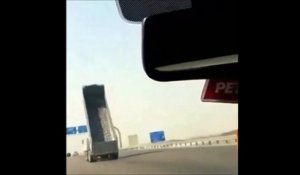 Un camion avec la remorque levée passe sous un pont sur l'autoroute